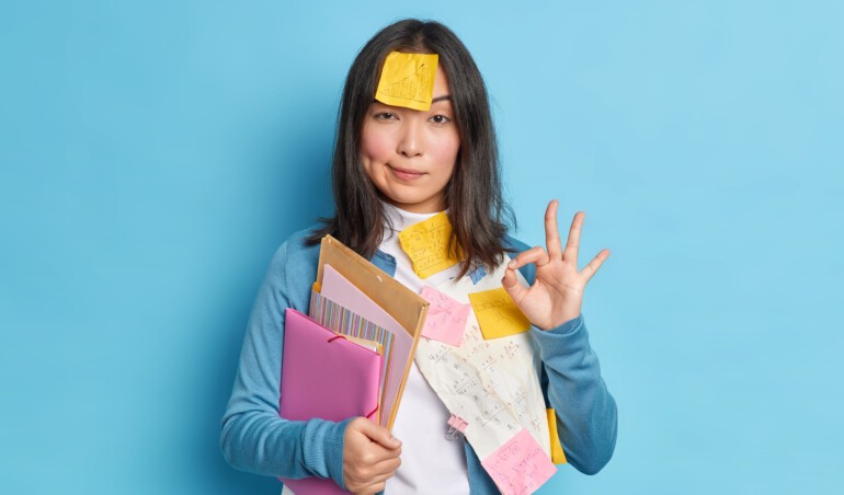 everything is control serious self confident young asian woman makes okay gesture agrees collaborate with colleague preparing research work surrounded with papers stickers